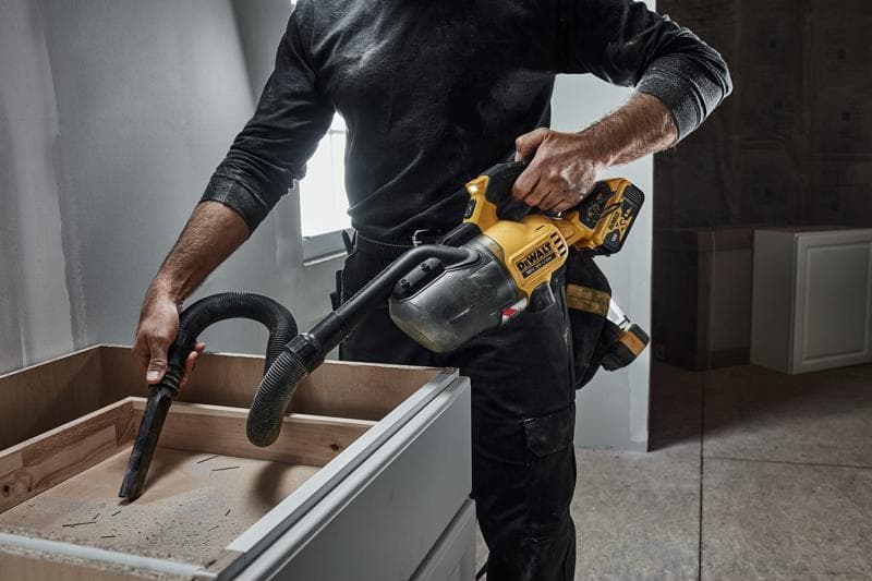 Person uses a DEWALT cordless handheld vacuum to clean dust from a wooden cabinet during construction.