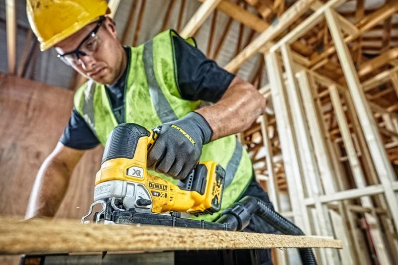 DEWALT DCS334P2 jigsaw used for cutting wood at a construction site by a worker wearing safety gear.
